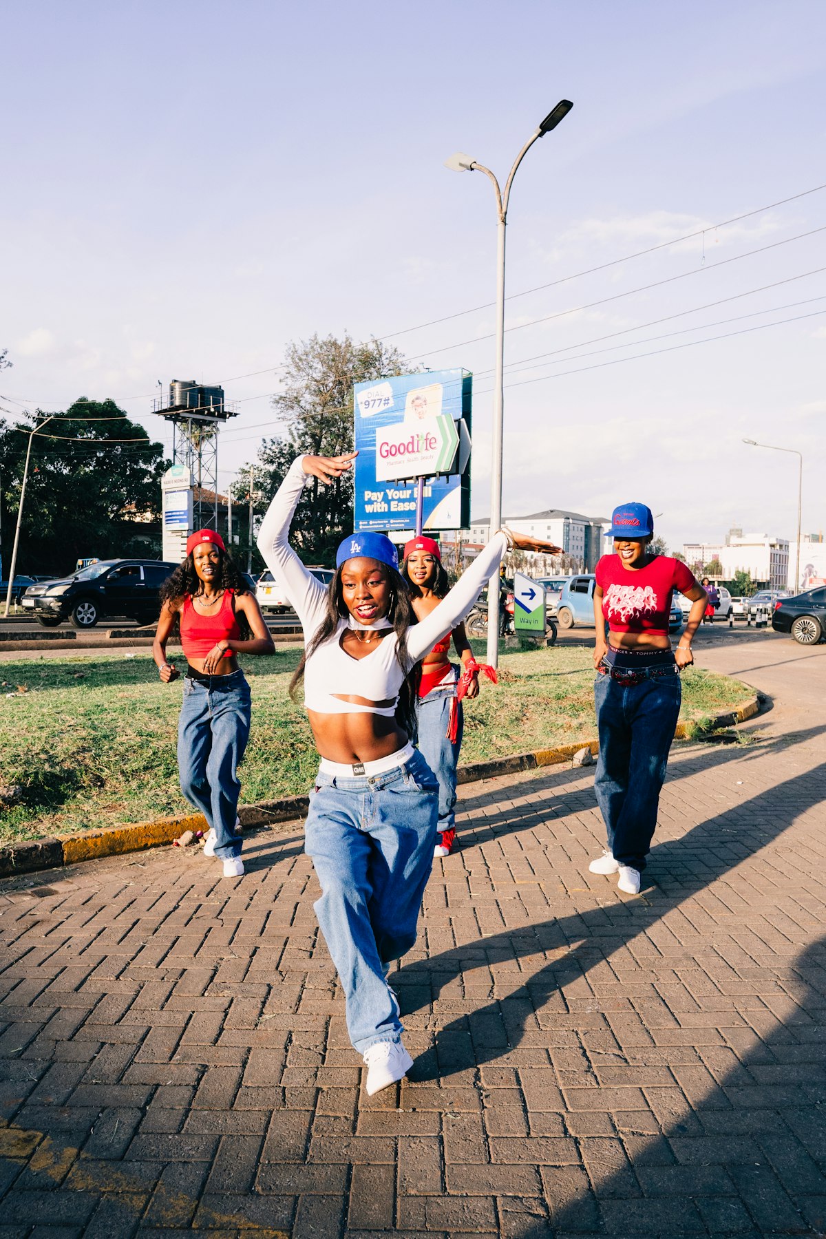 Four dancers in red and blue moving down a city street in sunlight